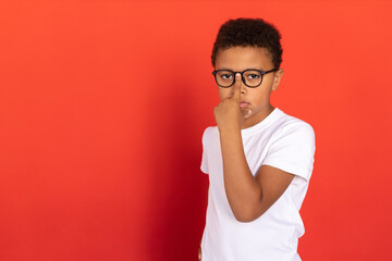 Portrait of clever preteen boy adjusting eyeglasses on nose. Mixed race preteen schoolboy wearing white T-shirt looking at camera against red background. Education concept