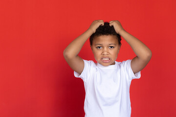 Portrait of worried preteen boy scratching head. Mixed race child wearing white T-shirt standing...
