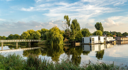 Obraz premium Village of Halfweg, municipality of Haarlemmermeer, The Netherlands, view of the wooden bridge and houseboats along the canal