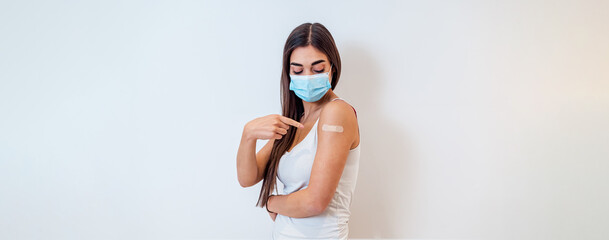 Healthy adult young woman, wearing a mask, pointing at the bandage after vaccine.
