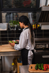 Fototapeta premium african american chef in apron holding bowl with lettuce.