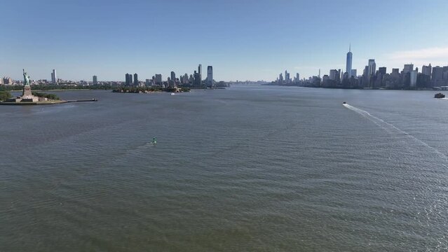 An aerial view of New York Harbor on a sunny day with clear blue skies. The drone camera truck right viewing the Statue of Liberty, New Jersey and lower Manhattan in the distance.