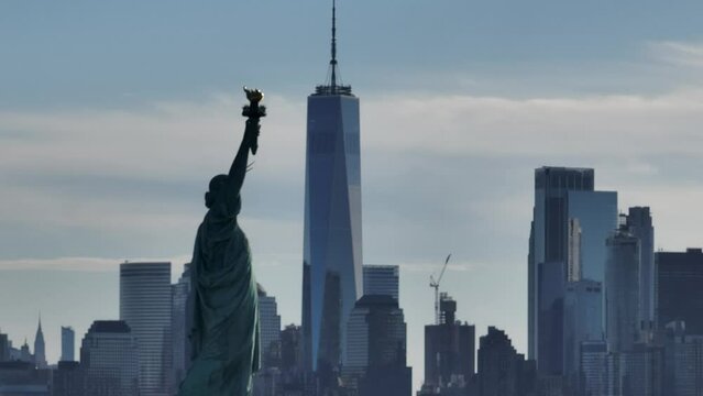 An aerial view of the Statue of Liberty with the freedom tower in the background on a beautiful morning. The camera truck right and boom up while zoomed in creating a parallax effect.