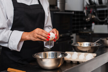 partial view of african american woman breaking raw egg above bowl while cooking in kitchen.