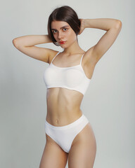 Fototapeta premium Young woman posing in a in white casual underwear on gray background in studio, copy space. Seductive woman perfect body. Sexy fashion model wear underwear.