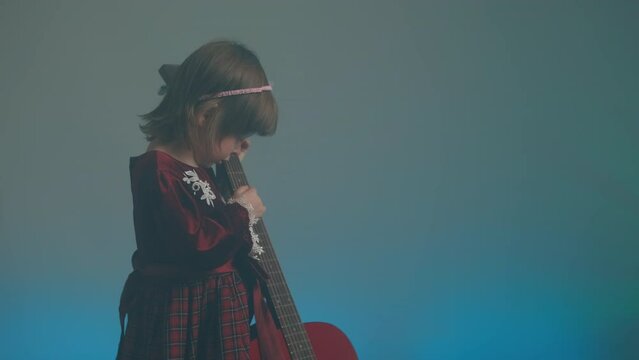 Cute little girl stands on stage in vintage dress and plays an acoustic guitar like a counter bass or cello. The concept of performing the author jazz and blues music. Hobbies and art among children