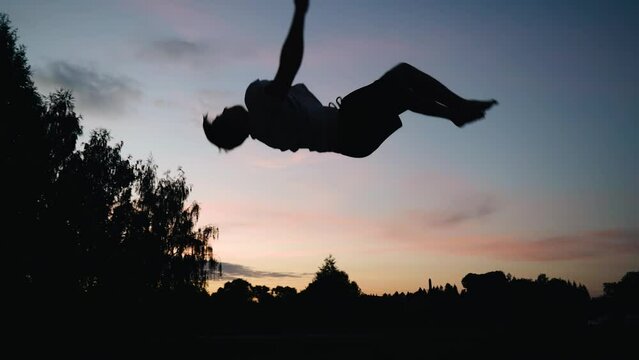 Against the background of the sunset, a guy jumps with a back flip. Slow-motion footage of the jump