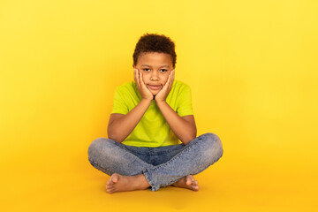 Portrait of happy preteen boy sitting crossing legs and looking at camera. Mixed race child wearing...