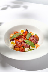 Salad with roast beef, vegetables and eggs on white table with harsh shadows. Steak salad in modern style with shadows of leaves. Flashy food. Meat salad with pastrami in summer menu.