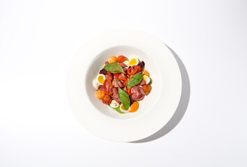 Salad with roast beef, vegetables and eggs on white table with harsh shadows. Steak salad in modern style with shadows of leaves. Flashy food. Meat salad with pastrami in summer menu.