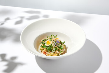 Healthy salad with squid and avocado on white plate with harsh shadows. Calamari salad with vegetables and eggs on white background with shadows of leaves. Summer food menu.