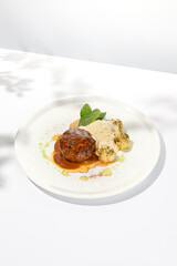 Beef cutlet with grilled cauliflower with gravy and cheese sauce on white plate. Elegant beefsteak on light background with shadows of sunlight. Summer menu with hard shadows Meat ball of minced meat