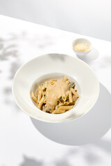 Italian pasta penne with chicken and mushrooms in creamy sauce. Mushroom and chicken pasta on white plate with shadows of sunlight. Summer italian lunch Penne with mushroom sauce on light background