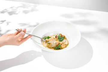 Woman hand holding fork with sea scallop over creamy risotto. Person eat seafood risotto with...