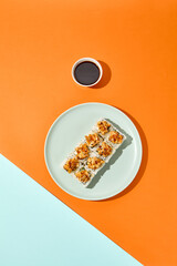 Baked maki sushi in ceramic plate on coloured background. Sushi roll with shrimp tartare in trendy style on orange and blue colour backdrop Maki roll with hard shadows in minimal style © Ryzhkov