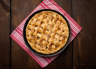 Round baked apple pie on a brown wooden table, top view