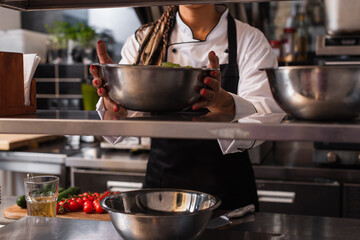 cropped view of tattooed african american chef holding bowl in professional kitchen.