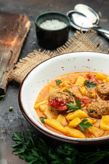 stew called lecho meatball, potato, onion, zucchini with tomato sauce, garlic and herbs in a white bowl, vertical image. top view. place for text