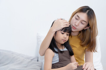Asian Caring Mother holding her sick daughter and measuring temperature with her hand.