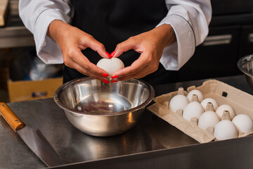 cropped view of african american chef holding raw egg above bowl while cooking in kitchen.