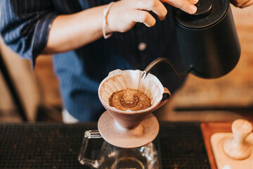Professional barista making filtered drip coffee in coffee shop. Close up of hands barista brewing a drip hot espresso coffee, pour over coffee with hot water and filter paper in coffee cafe.