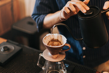 Professional barista making filtered drip coffee in coffee shop. Close up of hands barista brewing a drip hot espresso coffee, pour over coffee with hot water and filter paper in coffee cafe.