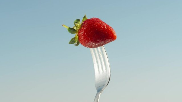 A strawberry, impaled on a fork, rotates against the background of a blue sky. close-up