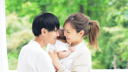 Fototapeta premium 新緑を背景に赤ちゃんを抱っこするカップル 子育てイメージ