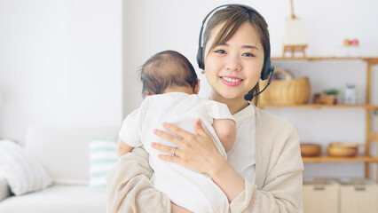 Obraz na płótnie Canvas 赤ちゃんを抱っこしながらビデオ通話で話す女性