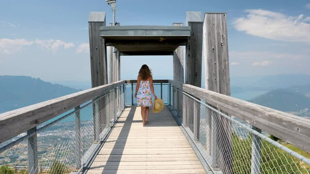 Woman walking on wooden bridge to viewpoint - panoramic landscape view (France, Savoie)