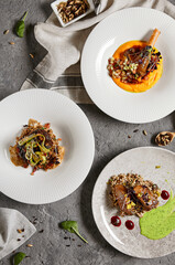 Set with main courses. Composition with meat dishes on gray stone table and textile in contemporary style. Roasted beef tongue with pearl barley; beef cheeks and leg of lamb in restaurant menu.