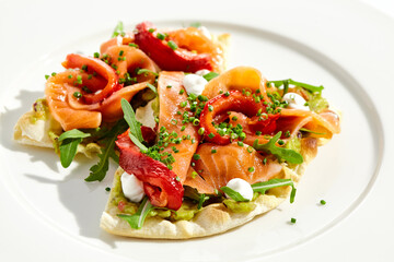 Bruschetta with salmon, avocado and paprika on white plate. Salmon bruschetta on crispy focaccia. Appetizer with guacamole, trout, cheese and paprika on toast. Fish antipasti in restaurant menu.