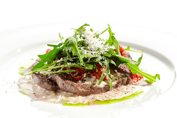 Meat medallions with mushroom creamy sauce and rucola salad on white background Meat steak on mushroom gravy with tomato and rocket salad. Roasted beef fillet with vegetables salad in restaurant menu.