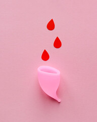 Menstrual cup and drops of blood on a pink background
