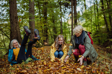 Happy little girl with mother and grandmother having fun with leaves during autumn walk in forest