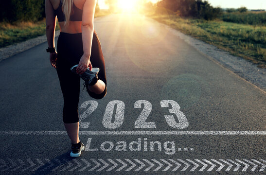 Sporty girl who is at the starting line to pass in 2023 year and the Loading bar drawn on asphalt. Concept of new professional achievements in the new year 2023 and success.
