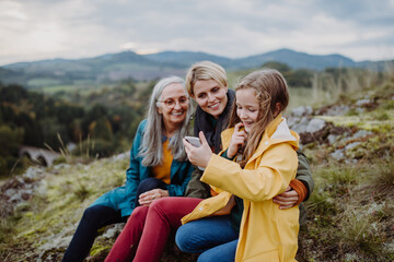 Small girl with mother and grandmother checking smartphone outoors on top of mountain.