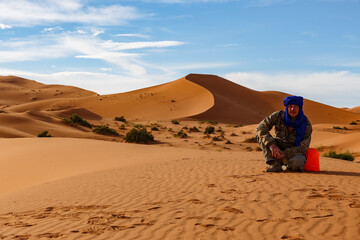 Fototapeta na wymiar Man sitting on sand dunes and looking at the camera. Sahara Desert. Erg Chebbi dunes in Morocco