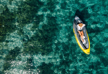 Fototapeta na wymiar A lonely female in a straw hat relaxing lying in floating inflatable kayak on the turquoise Adriatic Sea waves. Aerial coastal top view shot. Exotic countries vacations concept.