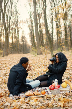 Loving black couple have a picnic in autumn park and take a photo