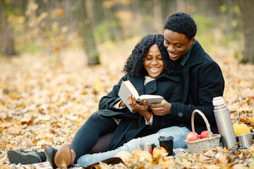 Loving black couple have a picnic in autumn park and reading a book