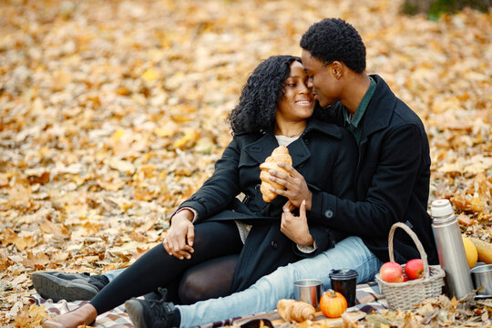Loving black couple have a picnic in autumn park and eating a croissant