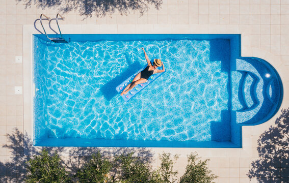 Sexy young female in swimsuit bikini, in a straw hat and sunglasses floating on blue swimming pool waves on inflatable mattress. Chill out summer vacation in luxury resorts concept.