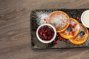 Three delicious pancakes with berries and fresh berry jam sauce with sugar decoration as dessert on...