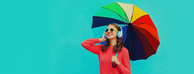 Autumn portrait of happy cheerful smiling young woman with colorful umbrella listening to music in...