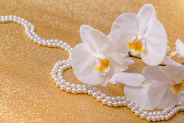 white Orchid and pearl necklace on a shiny gold background
