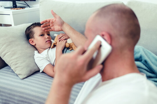 Worried man talking on smartphone while sitting near diseased son in the dedroom. Worried father consulting doctor on cellphone while sitting next to his little son in the living room.
