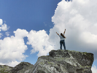 Hiker woman arms raised in the sky on mountain top summit above the clouds