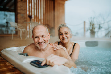 Senior couple enjoying together outdoor bathtub at their terrace during cold winter day.