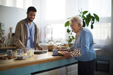 Young caregiver serving breakfast to elderly woman in nursing home care center.